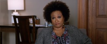 Movie still from “A Bad Moms Christmas” (2017), directed by Scott Moore – An older woman with an unkempt afro sits in front of a desk; Close Up shot, Over the shoulder angle