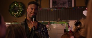 Movie still from “A Bad Moms Christmas” (2017), directed by Scott Moore – A man holding a microphone and smiling at the camera; Close Up shot, Over the shoulder angle