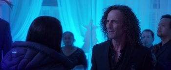 Movie still from “A Bad Moms Christmas” (2017), directed by Scott Moore – A man in a black suit standing in front of a blue background; Close Up shot, Over the shoulder angle