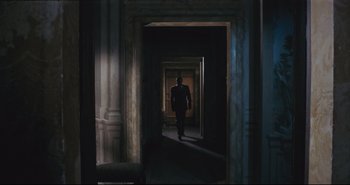 Movie still from “A Bay of Blood” (1971), directed by Mario Bava – A man in a suit walking through a dark hallway; Wide shot, Over the shoulder angle