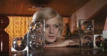 A woman is sitting at a table looking at her reflection in a mirror
