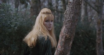 Movie still from “A Bay of Blood” (1971), directed by Mario Bava – A woman with long blonde hair standing next to a tree in the woods; Close Up shot, Low angle