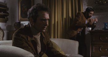 Movie still from “A Bay of Blood” (1971), directed by Mario Bava – A man sitting on top of a white couch next to a window; Medium shot, Low angle