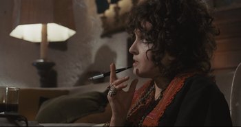Movie still from “A Bay of Blood” (1971), directed by Mario Bava – A woman smoking a cigarette while sitting in a chair; Close Up shot, Low angle