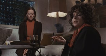Movie still from “A Bay of Blood” (1971), directed by Mario Bava – Two women sitting at a table with a cell phone; Medium shot, Low angle