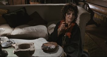 Movie still from “A Bay of Blood” (1971), directed by Mario Bava – A woman sitting on a couch holding a drink; Medium shot, High angle