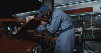 Movie still from “A Bay of Blood” (1971), directed by Mario Bava – A man working on an orange car in a garage; Medium shot, Low angle