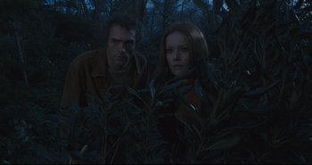 Movie still from “A Bay of Blood” (1971), directed by Mario Bava – A man and a woman standing next to each other in the woods; Medium shot, Low angle