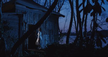 Movie still from “A Bay of Blood” (1971), directed by Mario Bava – A woman walking in front of a wooden house; Extreme Wide shot, Low angle