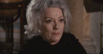 Movie still from “A Bay of Blood” (1971), directed by Mario Bava – An older woman with gray hair looking at the camera; Close Up shot, Over the shoulder angle
