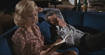 Movie still from “A Bay of Blood” (1971), directed by Mario Bava – A man and a woman sitting on a couch reading; Medium shot, High angle