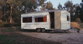 Movie still from “A Bay of Blood” (1971), directed by Mario Bava – A man standing in the doorway of an rv; Wide shot, High angle