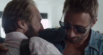 Movie still from “A Bigger Splash” (2015), directed by Luca Guadagnino – Two men in sunglasses are hugging each other; Close Up shot, Over the shoulder angle