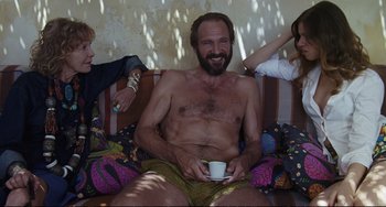 Movie still from “A Bigger Splash” (2015), directed by Luca Guadagnino – A man sitting on top of a couch holding a coffee cup; Medium shot, Over the shoulder angle