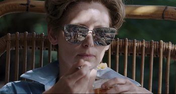 Movie still from “A Bigger Splash” (2015), directed by Luca Guadagnino – A woman sitting in a chair with a drink in her hand; Close Up shot, Over the shoulder angle