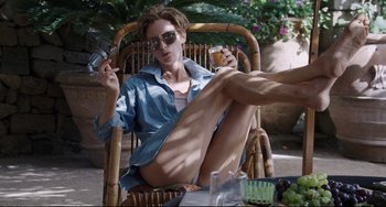 Movie still from “A Bigger Splash” (2015), directed by Luca Guadagnino – A woman sitting in a chair holding a glass of beer; Medium shot, High angle