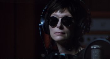 Movie still from “A Bigger Splash” (2015), directed by Luca Guadagnino – A woman with sunglasses and headphones is listening to music; Close Up shot, Over the shoulder angle