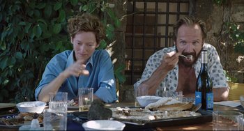 Movie still from “A Bigger Splash” (2015), directed by Luca Guadagnino – A man and a woman sitting at an outdoor table eating food; Medium shot, Over the shoulder angle