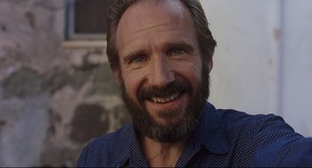 Movie still from “A Bigger Splash” (2015), directed by Luca Guadagnino – A person with a beard smiling; Close Up shot, Low angle