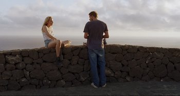 Movie still from “A Bigger Splash” (2015), directed by Luca Guadagnino – A man and a woman are sitting on a wall; Wide shot, Over the shoulder angle
