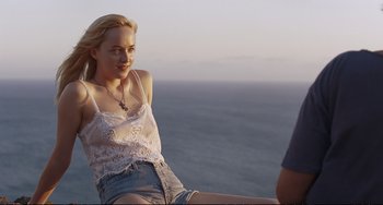 Movie still from “A Bigger Splash” (2015), directed by Luca Guadagnino – A woman sitting on a ledge near the ocean; Medium shot, Over the shoulder angle