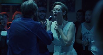 Movie still from “A Bigger Splash” (2015), directed by Luca Guadagnino – A man and a woman singing into microphones in front of a crowd; Medium shot, Over the shoulder angle
