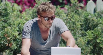 Movie still from “A Bigger Splash” (2015), directed by Luca Guadagnino – A man in a gray shirt is looking at a laptop; Medium shot, Low angle