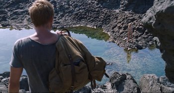 Movie still from “A Bigger Splash” (2015), directed by Luca Guadagnino – A person with a backpack standing next to a body of water; Wide shot, High angle
