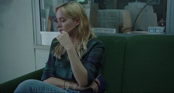 Movie still from “A Bigger Splash” (2015), directed by Luca Guadagnino – A woman sitting on top of a green couch holding a passport; Medium shot, Over the shoulder angle