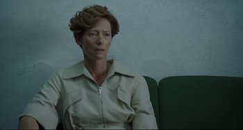 Movie still from “A Bigger Splash” (2015), directed by Luca Guadagnino – A woman sitting on a green couch in front of a white wall; Medium shot, Low angle