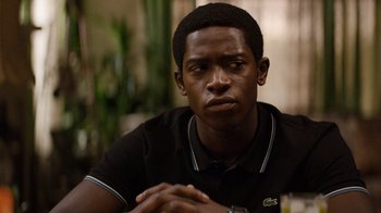 Movie still from “Snowfall” (2017), directed by Hiro Murai – A man sitting in front of a table with his hands crossed; Close Up shot, Over the shoulder angle