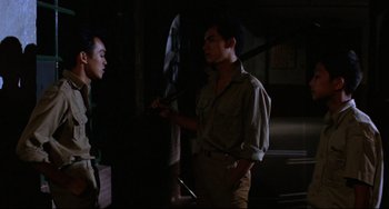 Movie still from “A Brighter Summer Day” (1991), directed by Edward Yang – A man holding an umbrella talking to another man in a dark room; Medium shot, Over the shoulder angle