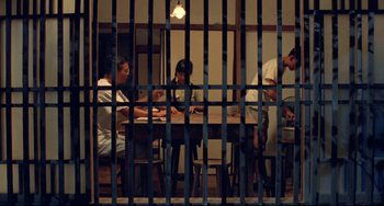 Movie still from “A Brighter Summer Day” (1991), directed by Edward Yang – A group of people sitting at a table in front of a jail cell; Wide shot, High angle