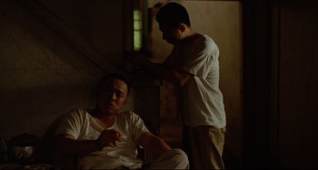 Movie still from “A Brighter Summer Day” (1991), directed by Edward Yang – A man sitting in a chair next to another man in a white shirt; Medium shot, High angle