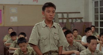 Movie still from “A Brighter Summer Day” (1991), directed by Edward Yang – A young man in a tan shirt is standing in front of a group of other young men; Medium shot, Over the shoulder angle