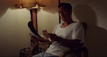 Movie still from “A Brighter Summer Day” (1991), directed by Edward Yang – A man sitting in front of a lamp holding a pair of shoes; Medium shot, High angle