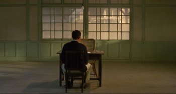 Movie still from “A Brighter Summer Day” (1991), directed by Edward Yang – A man sitting in front of a desk in front of a window; Wide shot, Low angle