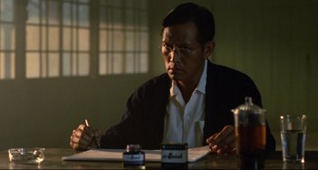 Movie still from “A Brighter Summer Day” (1991), directed by Edward Yang – A man sitting at a table writing on a piece of paper; Medium shot, Over the shoulder angle