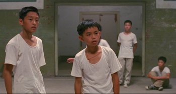 Movie still from “A Brighter Summer Day” (1991), directed by Edward Yang – A young boy in a white shirt is looking at the camera; Medium shot, Low angle