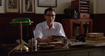 Movie still from “A Brighter Summer Day” (1991), directed by Edward Yang – A man sitting at a table holding a book; Medium shot, Low angle