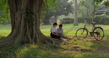 Movie still from “A Brighter Summer Day” (1991), directed by Edward Yang – Two people sitting on the ground under a tree; Wide shot, High angle