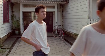 Movie still from “A Brighter Summer Day” (1991), directed by Edward Yang – A young man standing on the side of the street; Medium shot, Over the shoulder angle