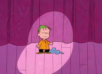 Movie still from “A Charlie Brown Christmas” (1965), directed by Bill Melendez – A charlie brown cartoon character is standing in front of a purple curtain; Extreme Wide shot, High angle