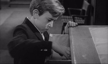 Movie still from “A Child Is Waiting” (1963), directed by John Cassavetes – A young boy in a black jacket is looking at a piece of paper; Medium shot, High angle