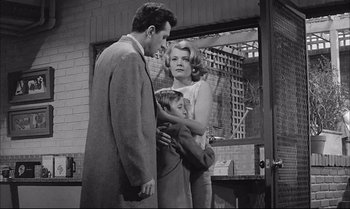 Movie still from “A Child Is Waiting” (1963), directed by John Cassavetes – A man and a woman and a child standing in front of a building; Medium shot, Low angle