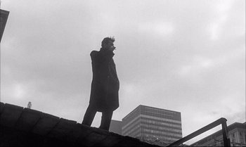 Movie still from “A Child Is Waiting” (1963), directed by John Cassavetes – A man standing on top of a building in front of some buildings; Wide shot, Low angle