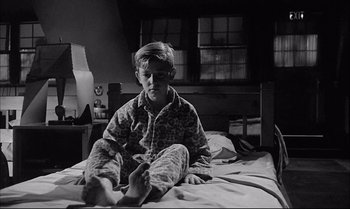 Movie still from “A Child Is Waiting” (1963), directed by John Cassavetes – A boy sitting on a bed in his pajamas; Medium shot, High angle