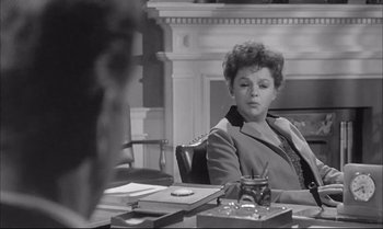 Movie still from “A Child Is Waiting” (1963), directed by John Cassavetes – A woman sitting at a table in a room; Medium shot, Over the shoulder angle