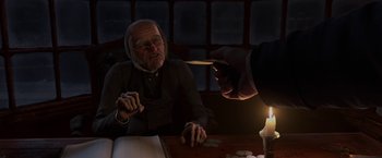 Movie still from “A Christmas Carol” (2009), directed by Robert Zemeckis – An old man sitting at a table in front of a lit candle; Medium shot, Over the shoulder angle