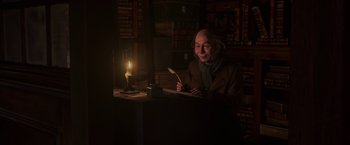 Movie still from “A Christmas Carol” (2009), directed by Robert Zemeckis – An old man sitting at a table with a candle in a dark room; Medium shot, High angle